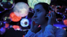 Woman wearing wireless black headphones and looking around in dark room of interactive museum or exhibition with colorful illumination. Immersive, futuristic, entertainment concept - Powered by Shutterstock - Get 15% off with code: PIKWIZARD15