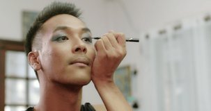 A charming short-haired Asian gay who owns a small beauty salon in the village is writing his eyeliner as he uses his mobile phone to record a video to post on social media.
