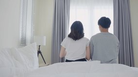 Rear view of Asian couple stretching hands after wakeup in morning. Attractive new marriage man and woman in pajamas feel happy and relax in the early day after get up from bed in bedroom together. - Powered by Shutterstock - Get 15% off with code: PIKWIZARD15