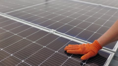 Unrecognizable man glove wiping solar panel from dust on sunny day. Close up of a young engineer hand is checking the operation of sun and cleanliness of photovoltaic solar panels on a sunset.