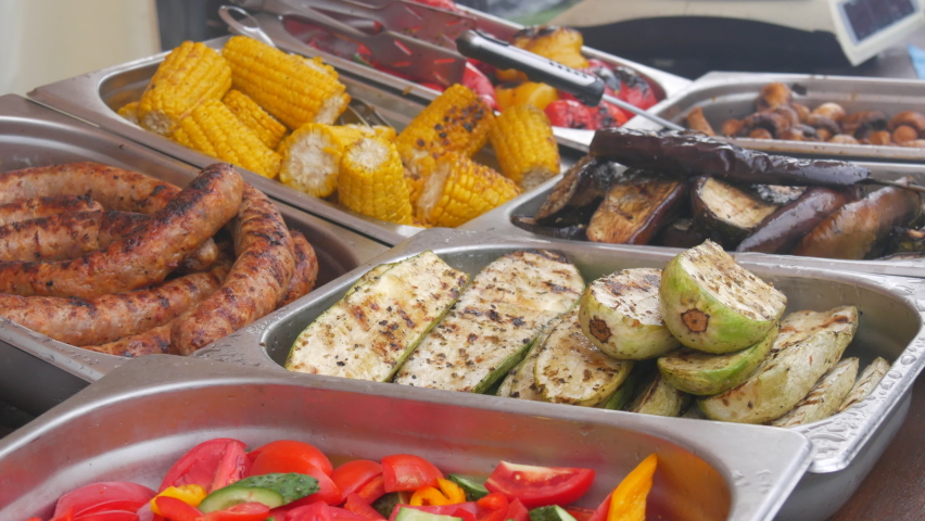 Grilled corn, sausage, eggplant and zucchini counter at outdoor street food festival. BBQ Shop for sale at the food festival. Street food ideas.