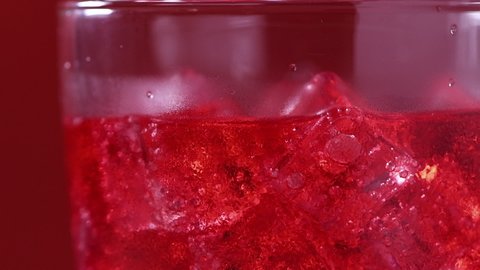 Pouring red soft drink into a glass full of ice cubes against red background, close-up slow motion shot. beverage and drink 