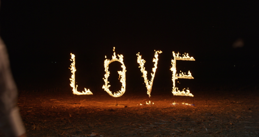 Portrait of a Young Affectionate Couple Kissing at Night With the Word LOVE in the Background Shining brightly with Fire. Man and Woman Celebrating their Anniversary with Big Letters Burning in Flames