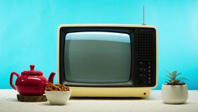 Close-up of old retro television on blue background, pressing buttons. Broken TV with grey interference screen and antenna, red teapot on table, bad signal reception, cinematography concept.