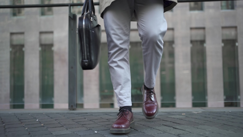 Young Trendy businessman walking in a modern corporate business district carrying leather briefcase while talking on cellphone. Casual executive professional having phone conversation in the city Royalty-Free Stock Footage #1079435168