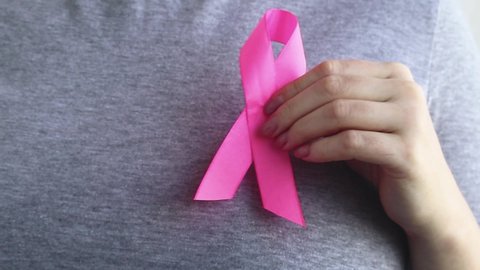 Breast Cancer Awareness Month. Woman attaches pink ribbon to her t-shirt. Support and help concept. Promotion of campaign against cancer.