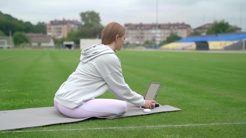 Slow motion, a girl puts on headphones and starts fitness training using a tablet at the stadium