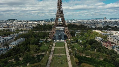 Drone reveal shot of the Eiffel tower in Paris on a partially cloudy day. Blue skies and city landscape in the background.