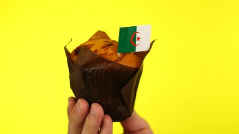 Cupcake with Algerian flag on male palm against yellow background