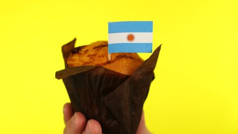 Cupcake with Argentinian flag on male palm against yellow background