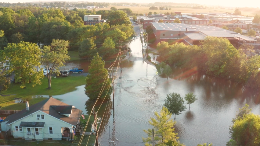 Flood river stream covers streets and roads in small town America, USA. Aerial drone revealing shot at golden hour morning sunrise.