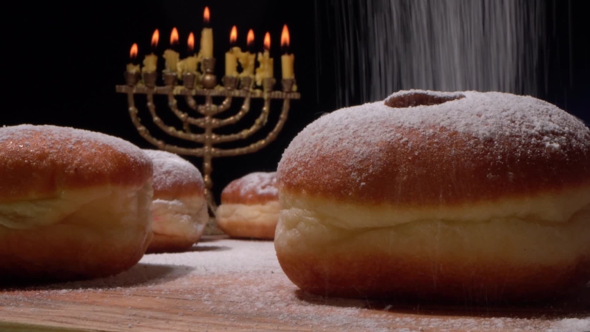 The Hanukkah menorah and lights. Sufganiyot are fried balls of yeast dough filled with strawberry jelly and dusted heavily with powdered sugar. Cooking of doughnuts Royalty-Free Stock Footage #1079452733