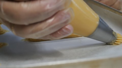 DOF, Dolly shot, close-up: A pastry chef's hand professionally squeezes the eclair custard dough onto a baking sheet from a pastry bag for baking in the oven. National desserts concept