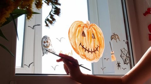 Child painting pumpkin on window preparing celebrate Halloween. Little kid draws decorates room interior with paper bats celebration autumn holiday at home Creative family leisure lockdown new reality. วิดีโอสต็อก