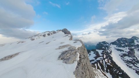 Beautiful landscape in the snowy mountain peaks taking by flying drone that getting up and down along the tops in high mountain range with little forest and stones under the cloudy sky
