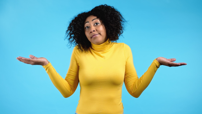 Young indifferent unsure african woman makes gesture of I don't know, can't help anything. Difficult question concept. Blue studio background. Royalty-Free Stock Footage #1079468624