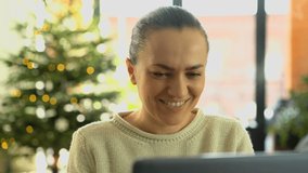 Young happy woman drinking coffee and chatting on tablet computer. Christmas tree in background
