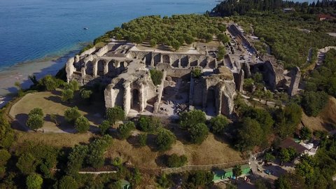 Cinematic 4K aerial drone rise and reverse shot of the Archaeological site of Grotte di Catullo in Sirmione, a tourist destination with a castle and a roman villa on the shores of Lake Garda in Italy