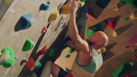 Strong Experienced Rock Climber Practicing Solo Climbing on Bouldering Wall in Gym. Man Exercising at Indoor Fitness Facility, Doing Extreme Sport for His Healthy Lifestyle Training. Close Up Portrait