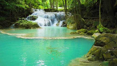 Waterfalls and fish swim in the emerald blue water in Erawan National Park. Erawan Waterfall is a beautiful natural rock waterfall in Kanchanaburi, Thailand.Onsen atmosphere. Fresh nature.4K