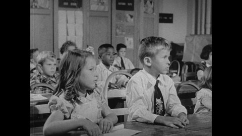 1950s: Classroom. Students hide under desks and cover heads. Teacher speaks. Little girls raises hand and stands. Girl speaks. Teacher points to chalkboard. Soldiers monitor skies on machine.