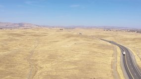 Drone slowly ascends and pans over a winding, desolate road through dry grasslands in California, USA.
