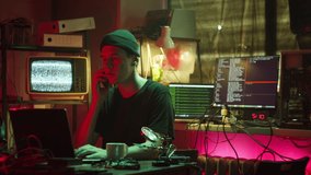 Young hacker typing on keyboard, breaking password, using laptop and talking on phone at night. Man developing program in dark room. Programmer answering on call, infecting system with cyber virus - Powered by Shutterstock - Get 15% off with code: PIKWIZARD15