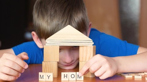 The child plays with blocks builds a house. The boy dreams of a new home. My home lettering made of cubes in the hands of a kid. selective focus, shallow depth of field