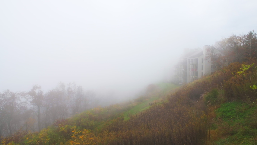 High angle aerial view in morning with foggy weather, season fog in Wintergreen Resort, Virginia ski town with condo apartment lodge buildings by Blue Ridge mountains meadow