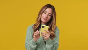 Young brunette woman 30s years old wears mint sweater hold use mobile cell phone swipe browsing doing online shopping order order delivery to home isolated on plain yellow background studio portrait