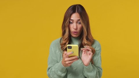 Shocked young brunette woman 30s wears mint sweater hold talk using mobile cell phone just found out great big win news doing winner gesture say yes isolated on plain yellow background studio portrait