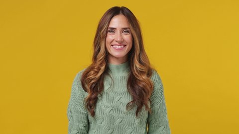 Smiling charming fascinating young brunette woman 30s years old wears mint sweater looking camera wink eye blink isolated on plain yellow background studio portrait. People emotions lifestyle concept