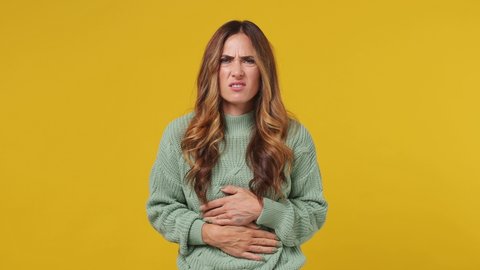 Sick tired young brunette woman 30s years old wears mint sweater put hands on abdomen suffering from stomach-ache griping bellyache feel bad seedy isolated on plain yellow background studio portrait