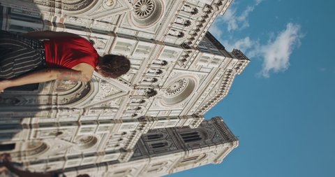 Vertical video of adorable asian woman tourist in red T-shirt and striped jeans walking near the magnificent historical building called Santa Maria del Fiore. Stylish hipster girl visiting Italy.