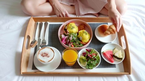 Room Service - Woman Eating Her Breakfast in Bed. Good Morning with Fresh Food on Tray. Woman Hand Eating French Croissant Sitting on Bed. Honeymoon Concept