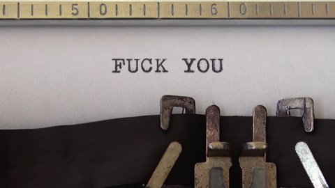 Typing phrase FUCK YOU on retro typewriter. Close up.