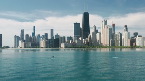 Man swimming on paddle board by Michigan lake with Chicago cityscape on motion background 4K. Cinematic aerial Chicago. Sunny summer day copy space on blue background. Modern water front buildings USA