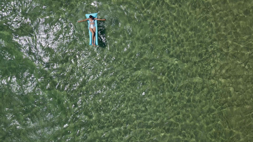 woman lies in a silver swimsuit on a blue inflatable mattress in the sea with clear water
