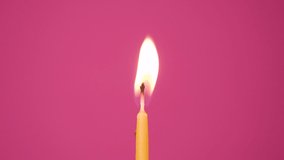 Blowing out cake candle burning on a pink background. Close up on blow out of yellow cake candle. Full HD resolution slow motion happy birthday or anniversary video.