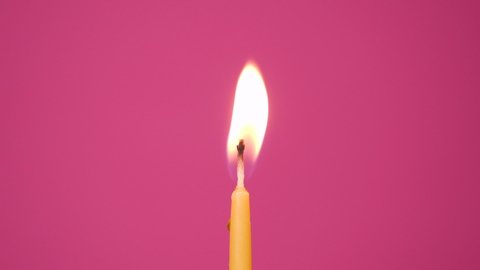 Blowing out cake candle burning on a pink background. Close up on blow out of yellow cake candle. Full HD resolution slow motion happy birthday or anniversary video.