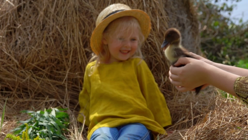 Cute little blond girl is looking at the little duckling at the woman