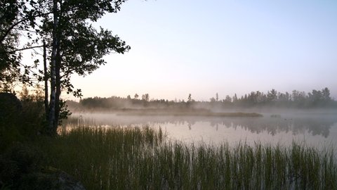 Fog floats over vast lake on cold, sunny early morning. Panning shot.