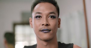 A smiling short-haired gay person who owns a small beauty salon in the village wearing false eyelashes and make up his face.