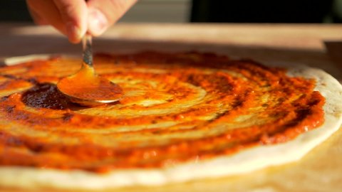Italian food restaurant chef baker cook spread tomato sauce of pizza pie pastry dish roasting. Spoon filling of tomatoes gravy on floured piece of dough before baking in oven. Tasty foodstuff cuisine.