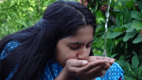 An Asian beautiful young girl is drinking water in the palm of her hand in on a hot day. Close-up view of a young girl is drinking water. Slow motion video.