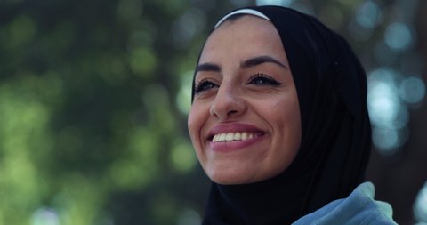 Cinematic close up shot of young happy arab woman wearing burqa is smiling in camera in green city park. Freedom of Arab woman and female rights