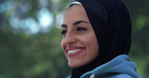 Cinematic close up shot of young happy arab woman wearing burqa is smiling in camera in green city park. 
