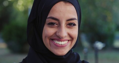 Cinematic shot of young happy arab woman wearing burqa is smiling satisfied with her results in camera on basketball outdoor court background after finishing a friendly game match.