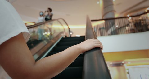 Close up on young woman hand holding on the escalator handrail. Asian woman's right hand holding the handrail and riding the escalator going up in the shopping mall.