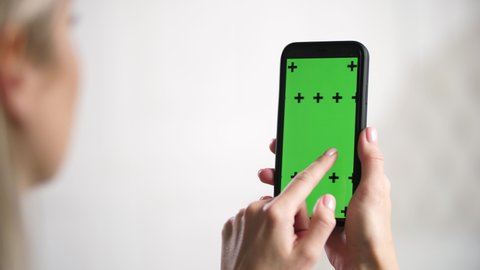 Closeup filming of green screen for ads on iPhone. Girl holds in hands smartphone device with moving green motion tracking points. Tapping mobile phone screen surface with fingers, swipers left right.